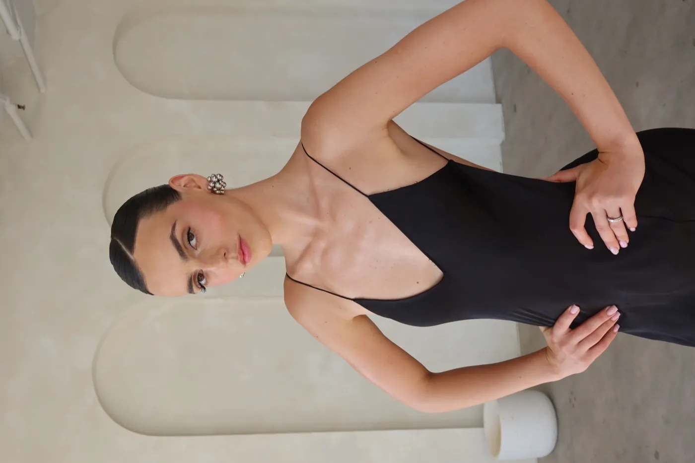 Model in a black slip dress with silver earrings in an arched room