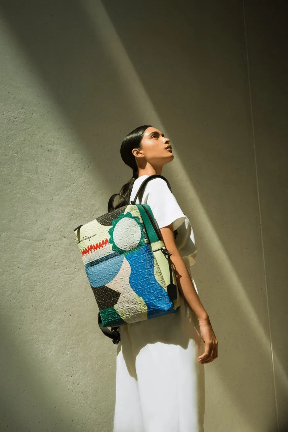 Model with a sleek low ponytail and a Salvatore Ferragamo capsule collection backpack in raking sunlight